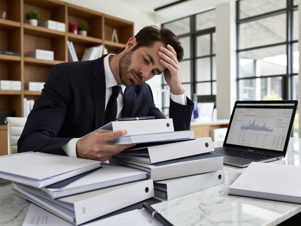 Overwhelmed business owner surrounded by multiple stacked office binders