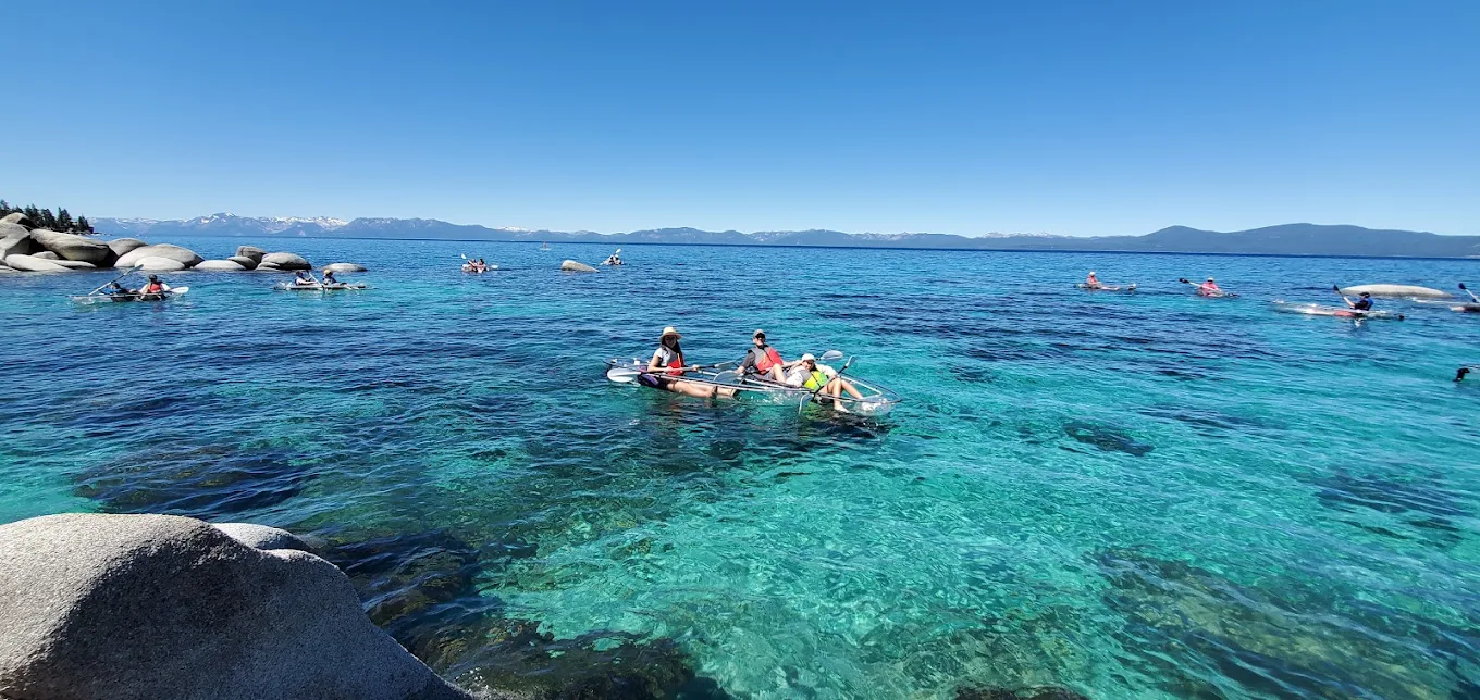 A wide aerial view of many clear kayaks scattered across bright turquoise water