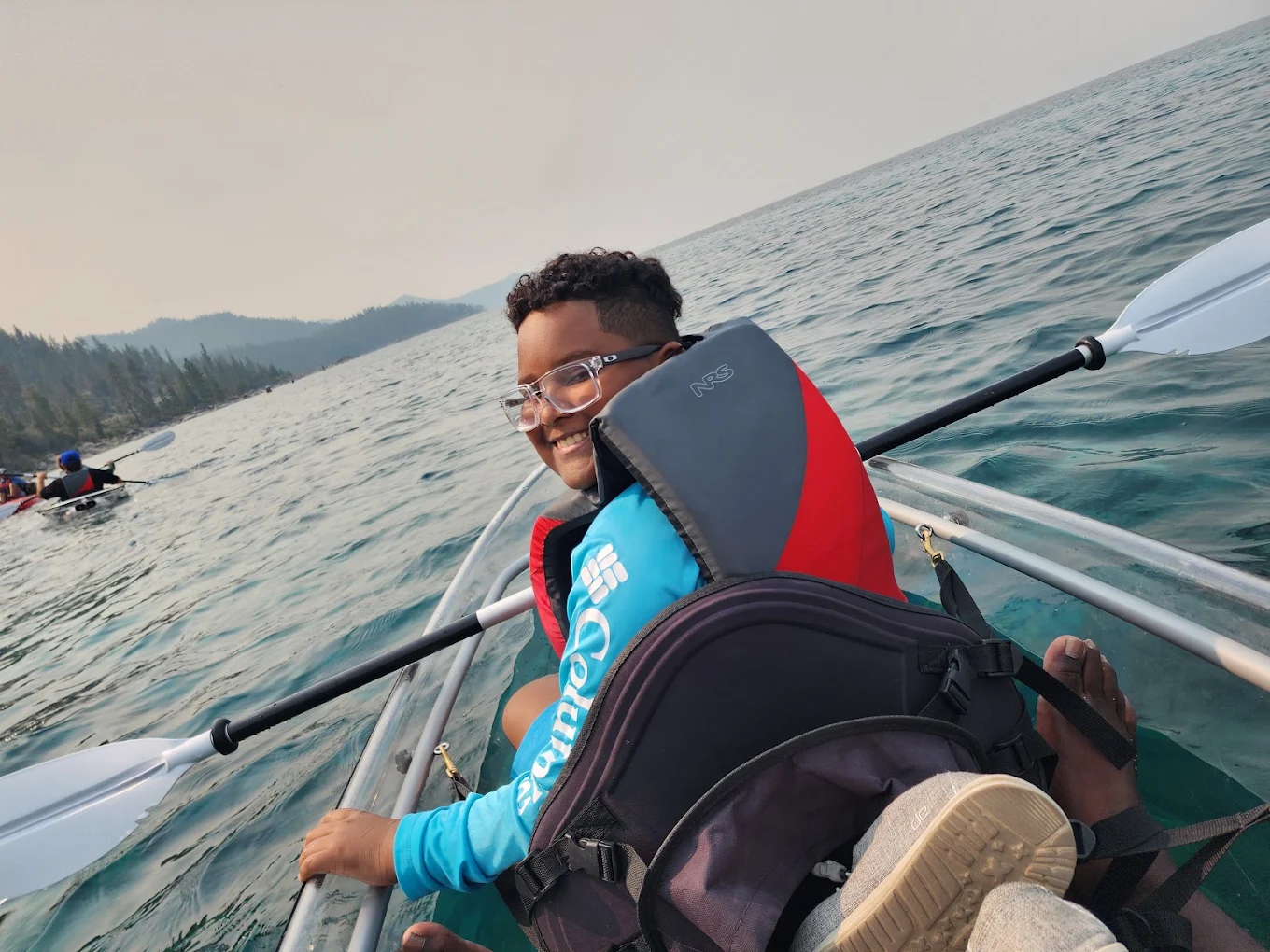 A young guest smiling while paddling a clear kayak on Lake Tahoe