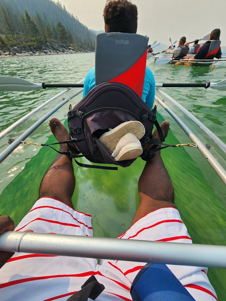 A point-of-view shot from inside a clear kayak over green-tinted water
