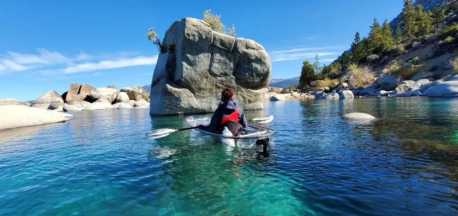 A guide paddling a clear kayak toward the granite formation at Bonsai Rock