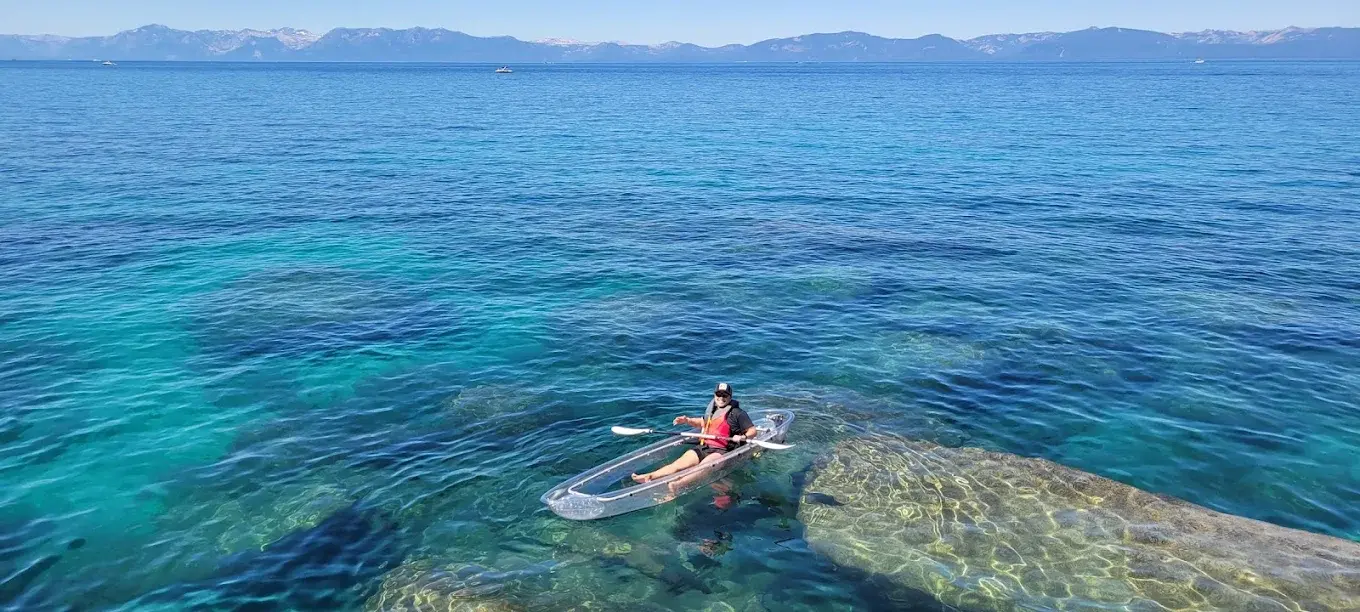 A single guest paddling their own fully transparent single clear kayak alone over deep blue Lake Tahoe water