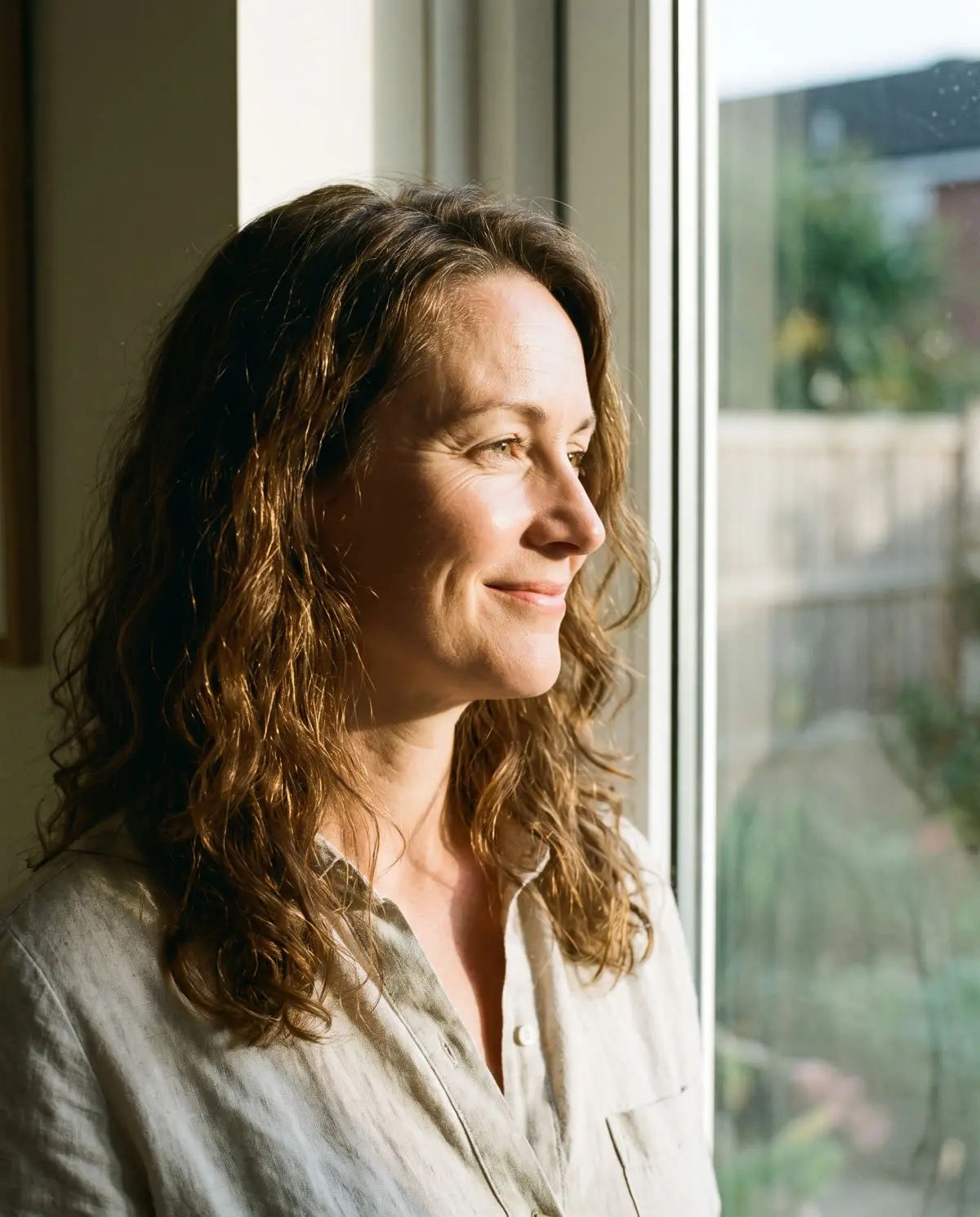 A woman smiling softly by a window in afternoon light