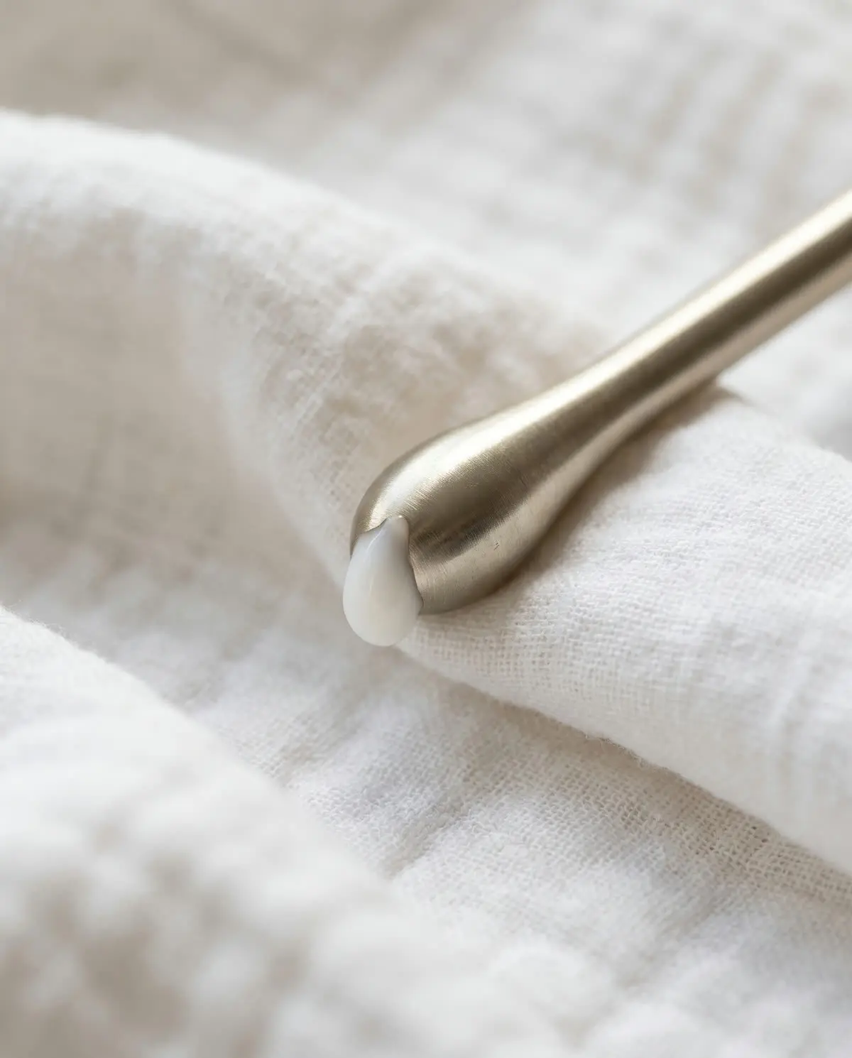 A gold-tone applicator tip with a droplet of cream